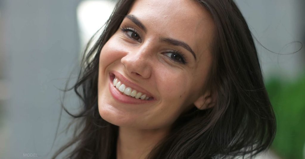 A white woman with brown hair is smiling and looking at the camera. (model)